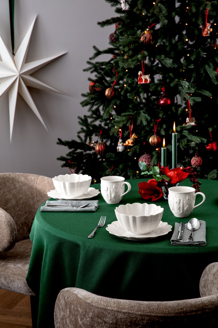 Frühstücksset auf einem festlich gedeckten Tisch mit grünem Tischtuch, im Hintergrund ein geschmückter Weihnachtsbaum. Perspektive von vorne.