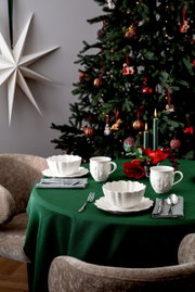 Frühstücksset auf einem festlich gedeckten Tisch mit grünem Tischtuch, im Hintergrund ein geschmückter Weihnachtsbaum. Perspektive von vorne.