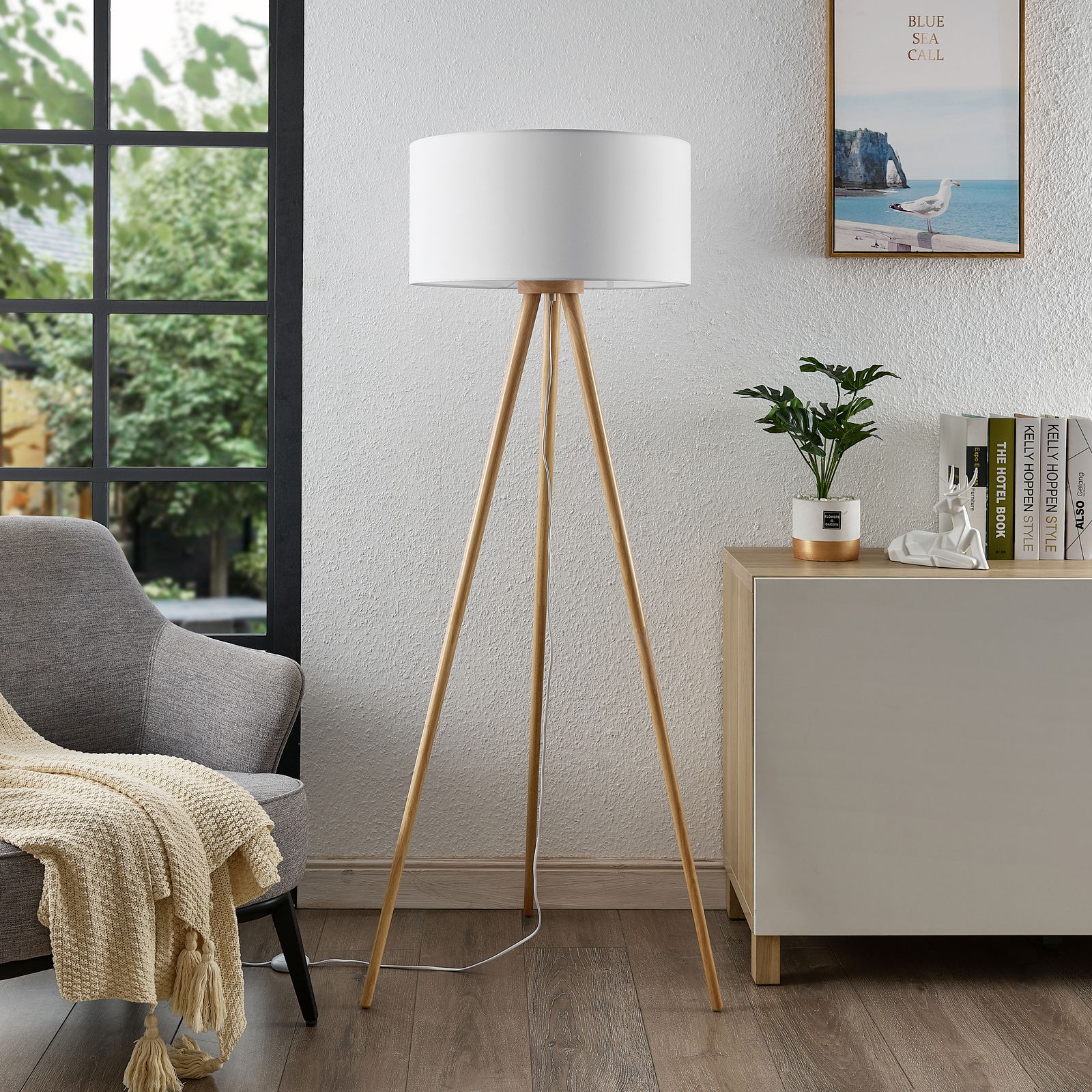 Moderne Stehleuchte mit dreibeinigem Holzgestell und weißem Lampenschirm, seitliche Perspektive im Wohnzimmer.