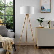Moderne Stehleuchte mit dreibeinigem Holzgestell und weißem Lampenschirm, seitliche Perspektive im Wohnzimmer.