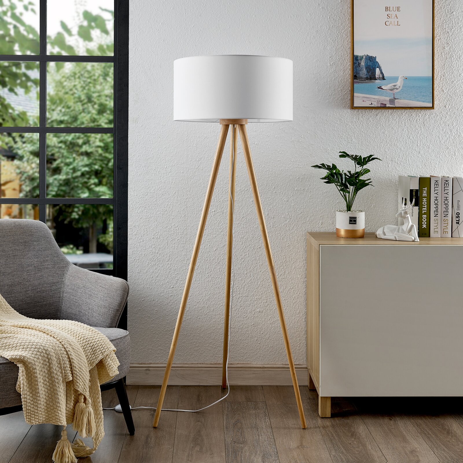Moderne Stehleuchte mit dreibeinigem Holzgestell und weißem Lampenschirm, seitliche Perspektive im Wohnzimmer.