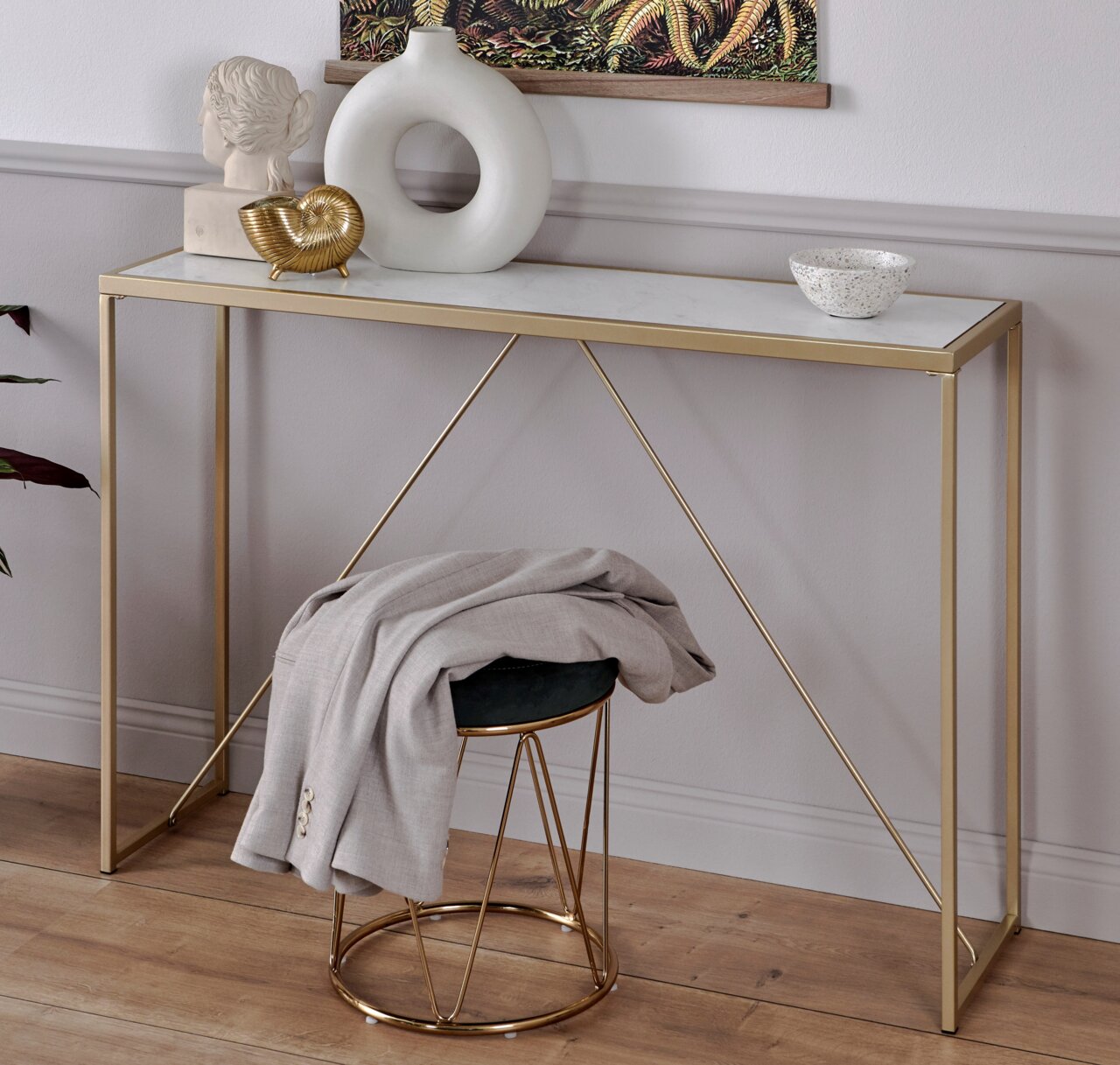 Moderner Konsolentisch mit goldenen Metallbeinen und weißer Tischplatte, dekoriert mit Skulpturen und einer Schale, seitliche Perspektive