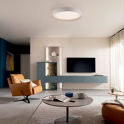 Modernes Wohnzimmer mit runder, weißer LED-Deckenleuchte; Ansicht aus leicht nach oben gerichteter Raum-/Frontperspektive mit TV-Wand und blauem Sideboard.