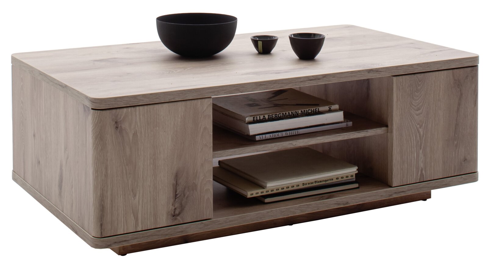 Rechteckiger Couchtisch aus hellgrauem Holzdekor mit abgerundeten Kanten und offenem Mittelregal mit Büchern, darauf schwarze Schalen; Ansicht schräg von vorne links.