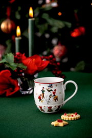 Weihnachtlicher Henkelbecher mit Schneemann-Motiv, umgeben von festlicher Dekoration, aus seitlicher Perspektive fotografiert.
