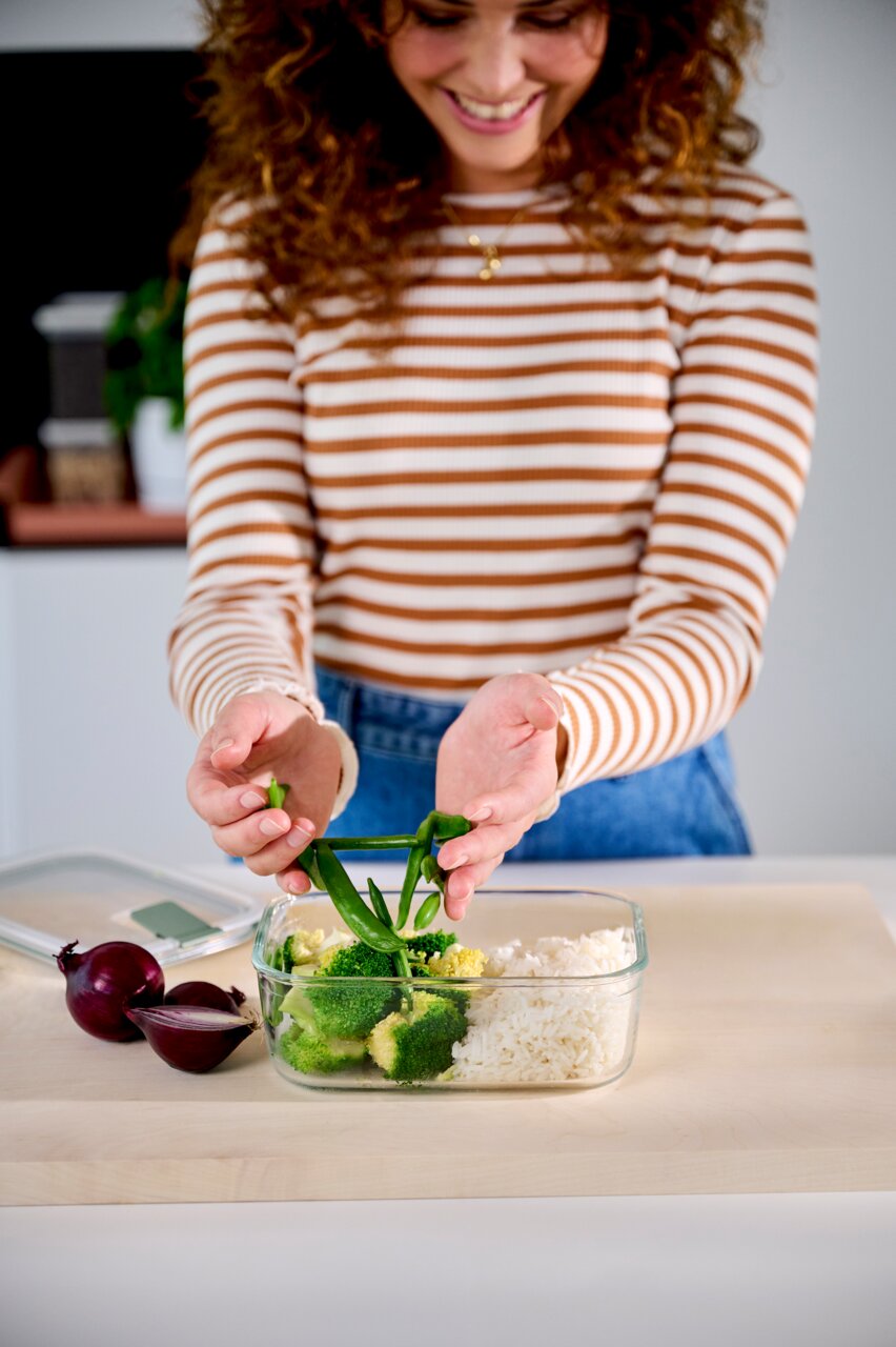 Frau füllt eine Glas-Frischhaltedose mit Gemüse und Reis, Ansicht von vorne.