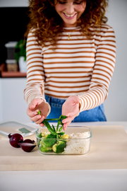 Frau füllt eine Glas-Frischhaltedose mit Gemüse und Reis, Ansicht von vorne.