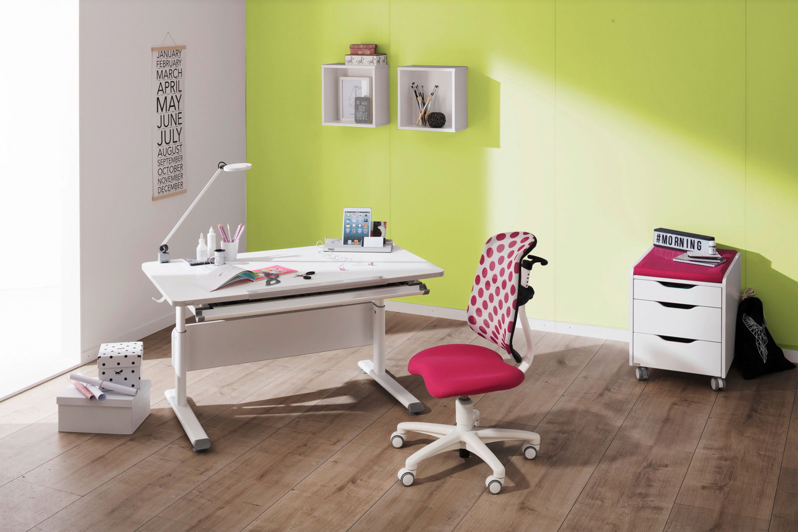 Moderner Schreibtisch mit weißer Oberfläche und verstellbarer Höhe, begleitet von einem pink gepunkteten Jugendstuhl, in einem hellen Raum mit grüner Wand, aus seitlicher Perspektive.