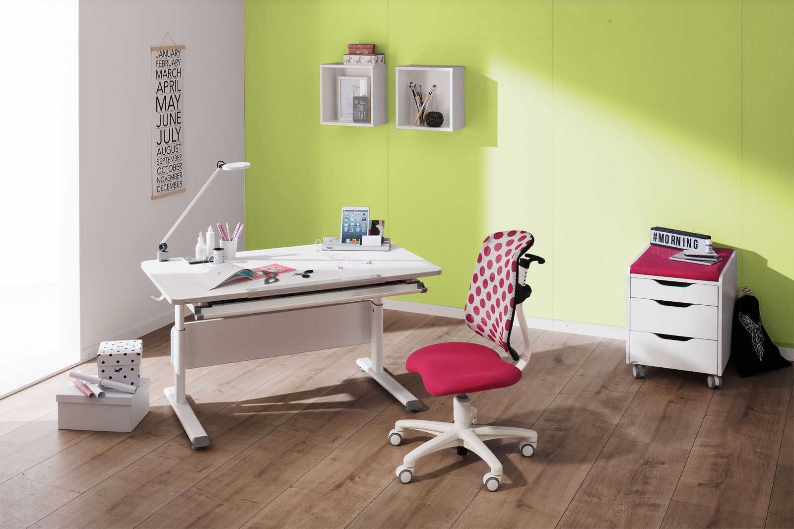 Paidi Schreibtisch DIEGO Moderner Schreibtisch mit weißer Oberfläche und verstellbarer Höhe, begleitet von einem pink gepunkteten Jugendstuhl, in einem hellen Raum mit grüner Wand, aus seitlicher Perspektive.