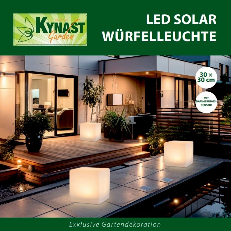 Solar Würfelleuchte 30x30cm auf einer Terrasse bei Nacht, leuchtend und umgeben von Pflanzen, mit moderner Architektur im Hintergrund.