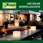 Solar Würfelleuchte 30x30cm auf einer Terrasse bei Nacht, leuchtend und umgeben von Pflanzen, mit moderner Architektur im Hintergrund.