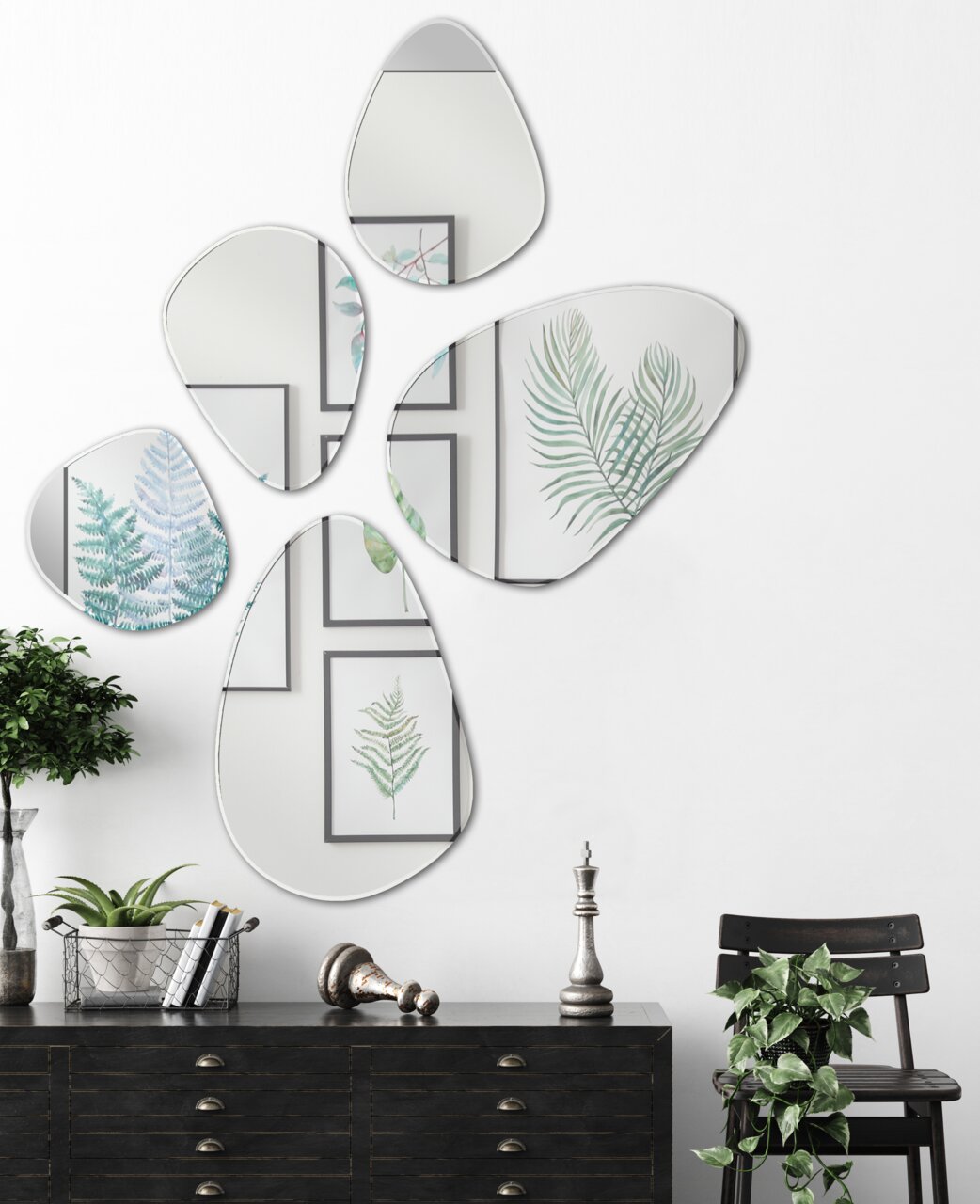 Fünf unregelmäßig geformte Facettenspiegel an einer weißen Wand, die Pflanzenbilder reflektieren, aus der Frontalperspektive betrachtet.