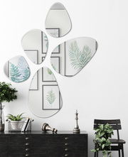 Fünf unregelmäßig geformte Facettenspiegel an einer weißen Wand, die Pflanzenbilder reflektieren, aus der Frontalperspektive betrachtet.