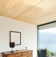 Moderne Tischleuchte mit schwarzem, gemustertem Lampenschirm auf einer Holzkommode, seitliche Perspektive mit Blick auf ein großes Fenster und Berglandschaft.