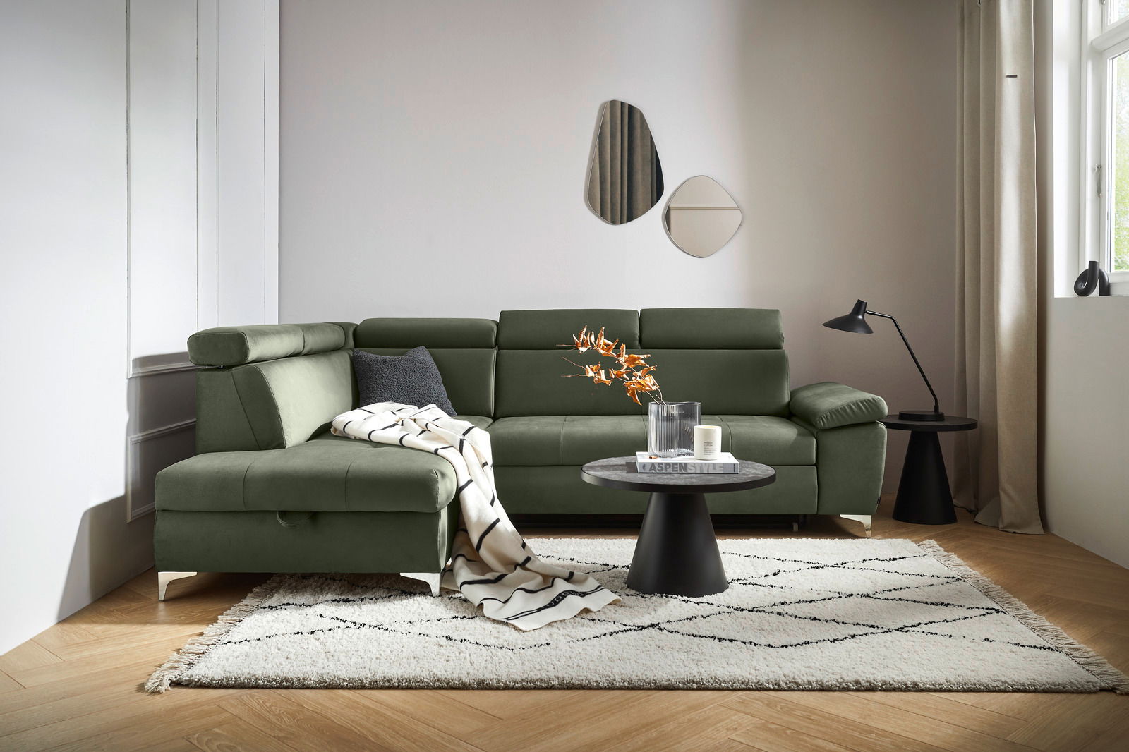 Osca Ecksofa RAUL Grüne Rundecke mit verstellbaren Kopfstützen, dekoriert mit Kissen und Decke, aus der Perspektive von vorne links fotografiert.