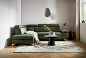 Grüne Rundecke mit verstellbaren Kopfstützen, dekoriert mit Kissen und Decke, aus der Perspektive von vorne links fotografiert.