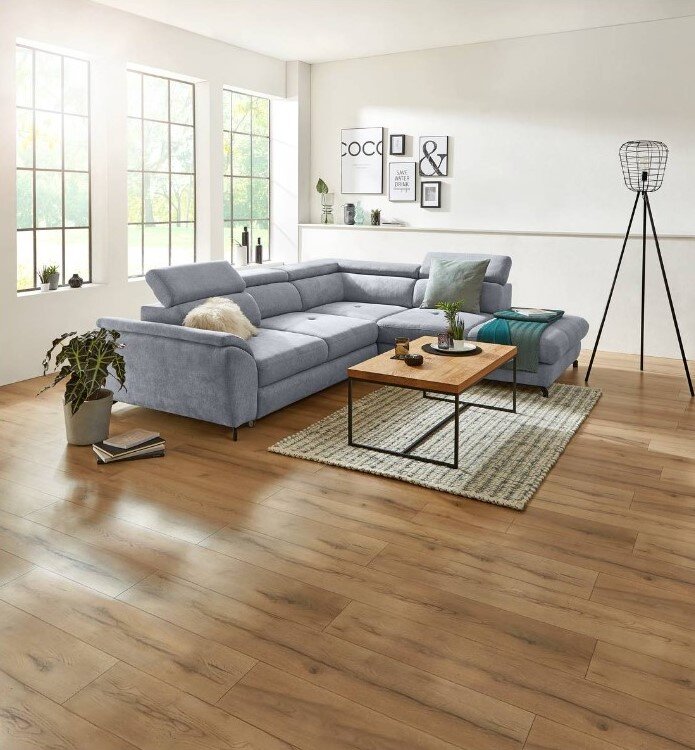 Grijze hoekbank MAROLA in een moderne woonkamer, zijaanzicht met houten vloer en grote ramen.