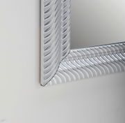 Nahaufnahme eines rechteckigen Spiegels mit dekorativem, wellenförmigem Rahmen in Silberoptik, perspektivisch von der Seite aufgenommen.