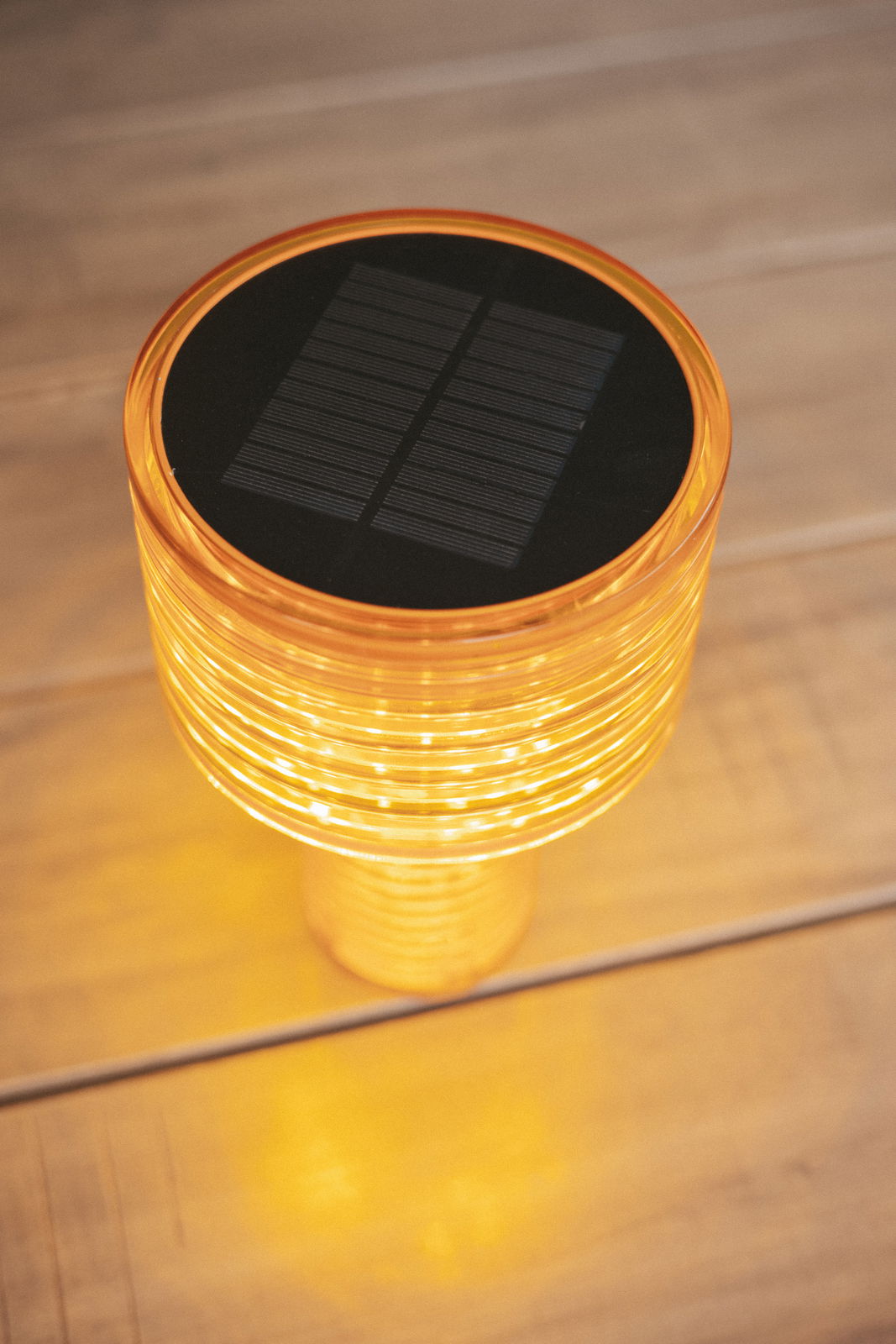 Obere Perspektive auf eine leuchtende Akku-Solar-Tischleuchte mit orangefarbenem Gehäuse und sichtbarem Solarpanel auf der Oberseite.
