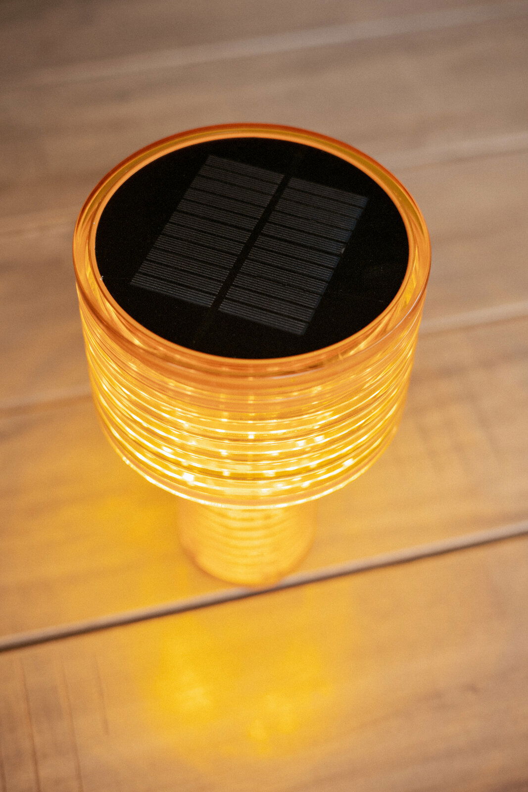 Obere Perspektive auf eine leuchtende Akku-Solar-Tischleuchte mit orangefarbenem Gehäuse und sichtbarem Solarpanel auf der Oberseite.