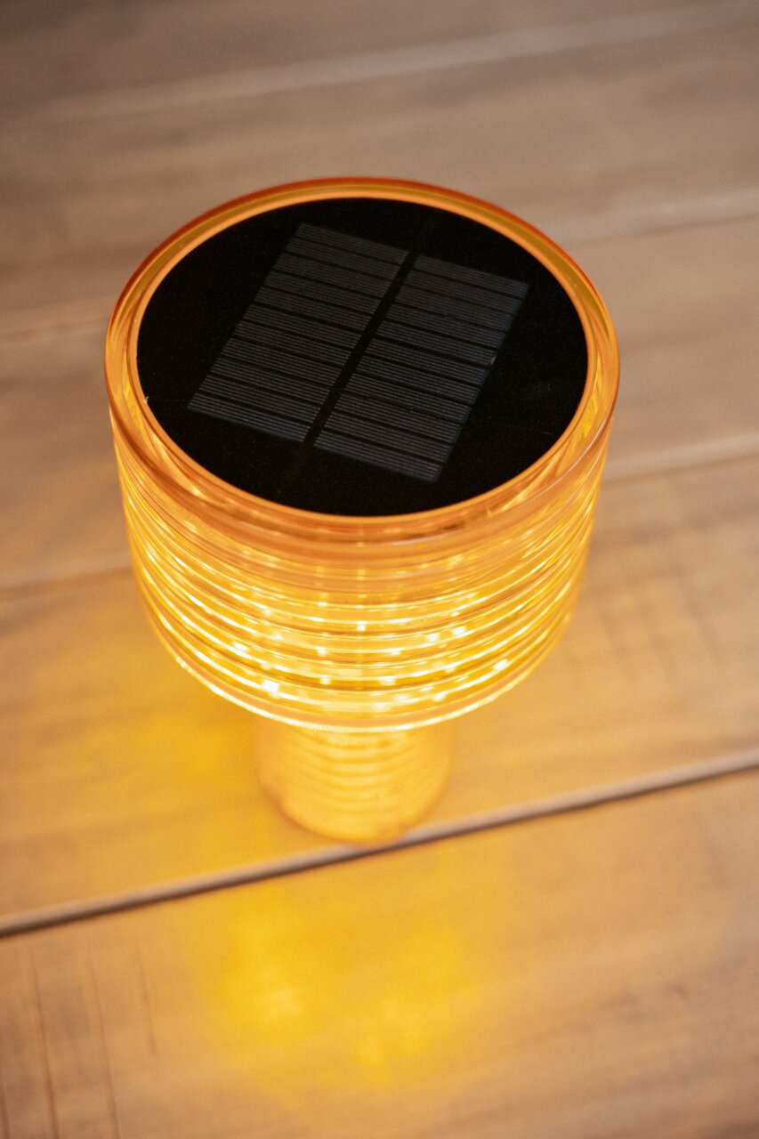 Obere Perspektive auf eine leuchtende Akku-Solar-Tischleuchte mit orangefarbenem Gehäuse und sichtbarem Solarpanel auf der Oberseite.