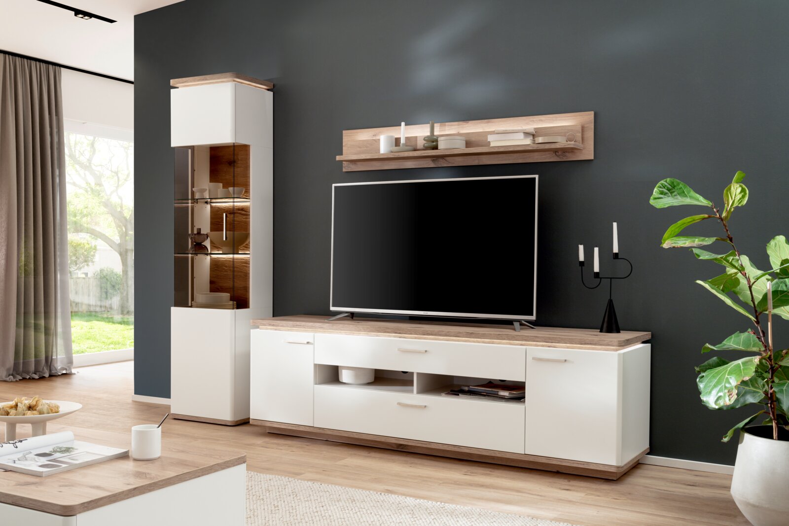 Modernes Wohnzimmer-Entertainment-Set in Weiß mit Holzoptik: Lowboard mit TV, passendem Wandregal und hoher Vitrine mit Glasfront, frontal aus leicht linksseitiger Perspektive aufgenommen