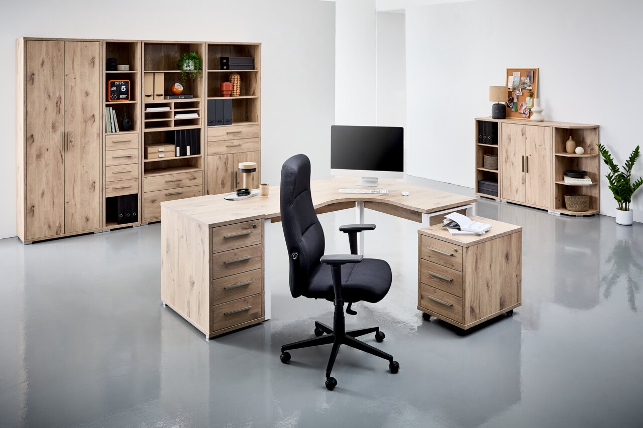 Moderne Büromöbel in Holzoptik, bestehend aus einem Eckschreibtisch mit Rollcontainer und einem ergonomischen Bürostuhl, umgeben von hohen Aktenschränken und Regalen. Perspektive: Frontalansicht.