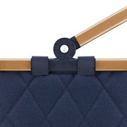 Nahaufnahme eines blauen, gesteppten carrybag XS mit braunem Griff und schwarzem Gelenk.