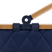 Nahaufnahme eines blauen, gesteppten carrybag XS mit braunem Griff und schwarzem Gelenk.