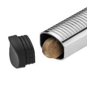 Nahaufnahme einer Muskatreibe aus Edelstahl mit einer Muskatnuss im Inneren, abnehmbare schwarze Kappe daneben.