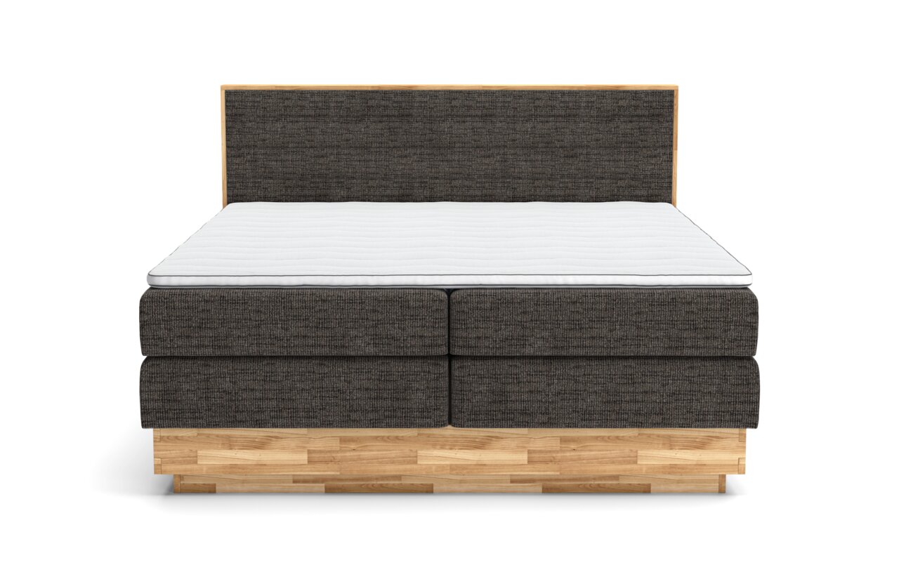 Vooraanzicht van een boxspringbed met een donkere stoffen bekleding en een licht houten frame.