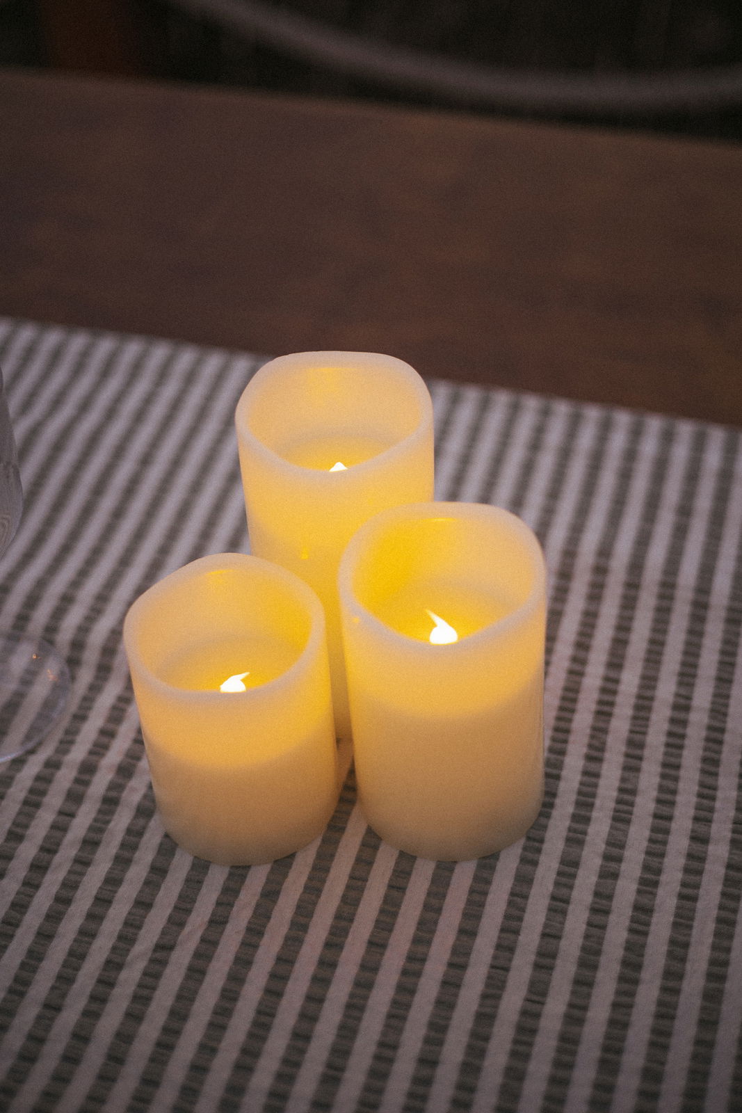 Drei leuchtende Outdoor-Kerzen auf einem gestreiften Tischläufer, aus der Vogelperspektive fotografiert.
