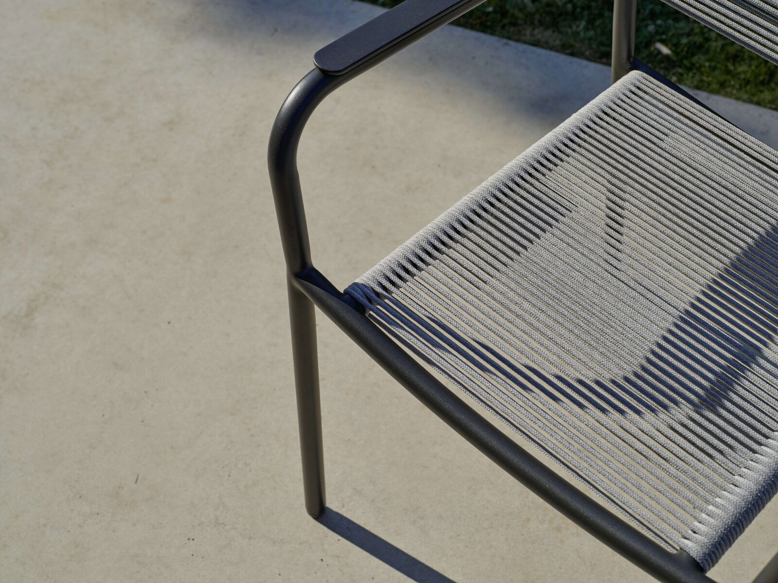 Nahaufnahme eines Stapelsessels mit Metallrahmen und geflochtener Sitzfläche, von oben betrachtet.