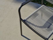 Nahaufnahme eines Stapelsessels mit Metallrahmen und geflochtener Sitzfläche, von oben betrachtet.