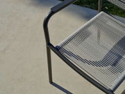 Nahaufnahme eines Stapelsessels mit Metallrahmen und geflochtener Sitzfläche, von oben betrachtet.