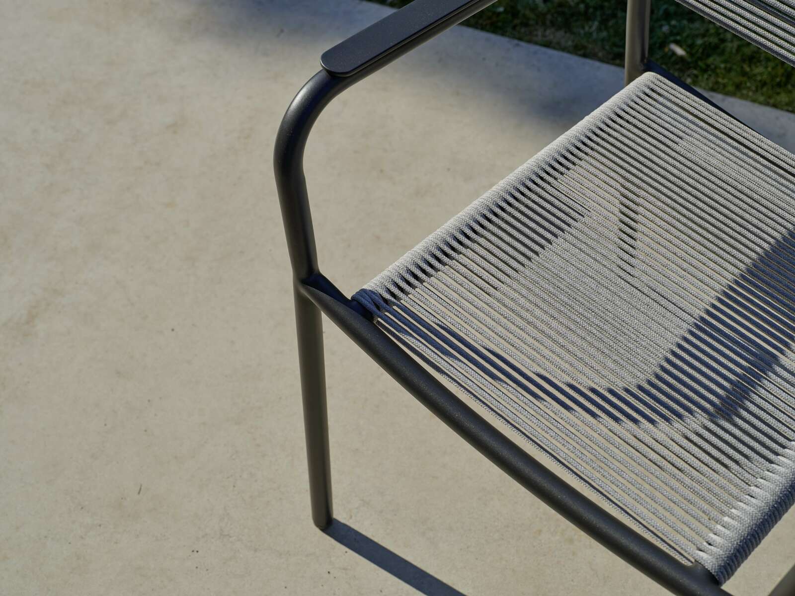 Nahaufnahme eines Stapelsessels mit Metallrahmen und geflochtener Sitzfläche, von oben betrachtet.