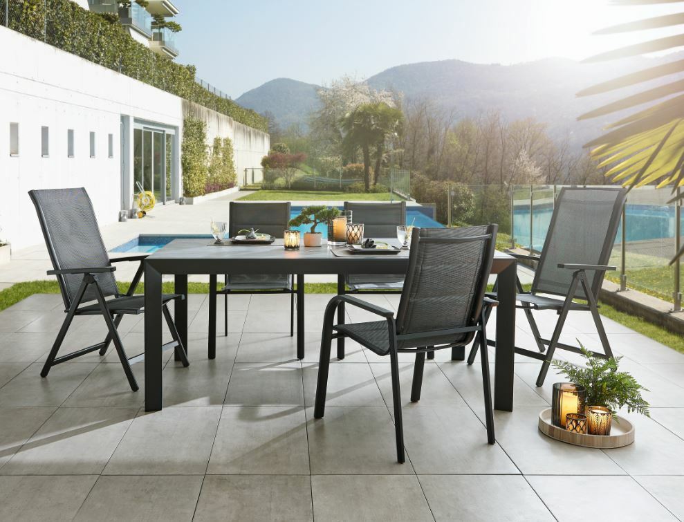 Moderner Gartentisch Ambia TERUEL mit vier Stühlen auf einer Terrasse, im Hintergrund ein Pool und Berge, seitliche Perspektive.