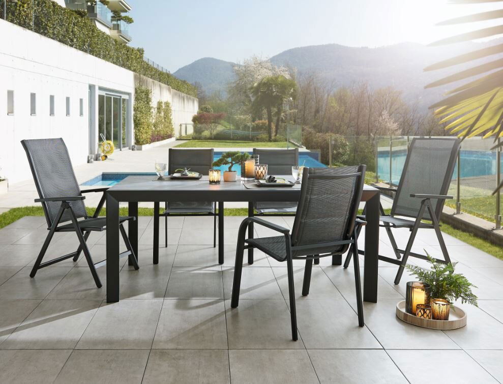 Moderner Gartentisch Ambia TERUEL mit vier Stühlen auf einer Terrasse, im Hintergrund ein Pool und Berge, seitliche Perspektive.