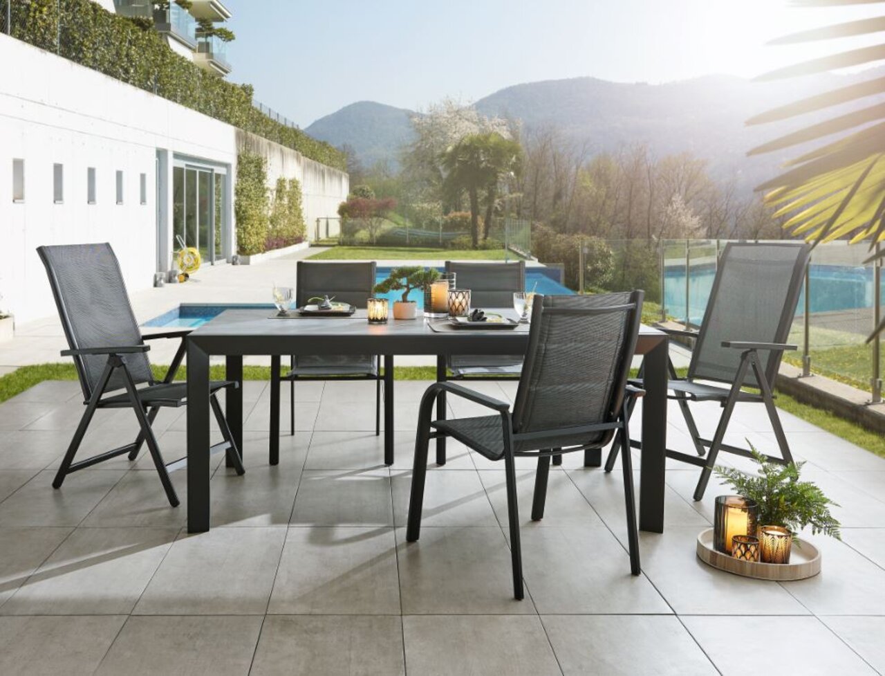 Moderne tuintafel Ambia TERUEL met vier stoelen op een terras, op de achtergrond een zwembad en bergen, zijaanzicht.