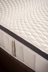 Nahaufnahme einer Matratze mit gestepptem Bezug und seitlichem Belüftungsstreifen, perspektivisch von der Seite aufgenommen.