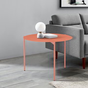 Runder Beistelltisch in Korallenfarbe, seitliche Perspektive, neben einem grauen Sofa, dekoriert mit einer Lampe und Büchern.