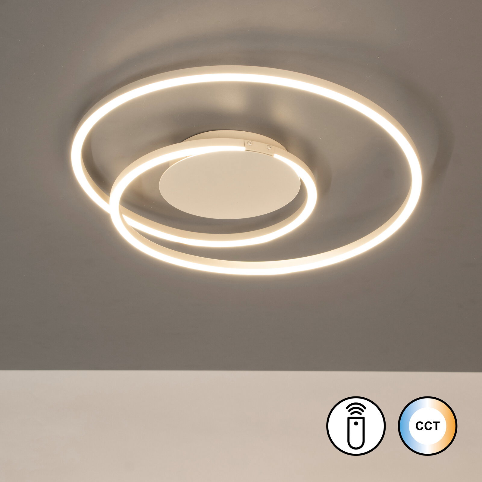 Moderne LED-Deckenleuchte mit zwei leuchtenden Ringen in warmweiß, Draufsicht von unten auf die an der Decke montierte Leuchte; Symbole für Fernbedienung und CCT-Farbtemperatursteuerung