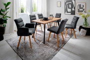 Moderner Esstisch mit Holzplatte und schwarzen Metallbeinen, umgeben von sechs grauen Polsterstühlen auf einem gemusterten Teppich in einem hellen Raum. Perspektive: seitlich von vorne.