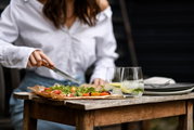 Iemand snijdt een pizza op een houten tafel; er staan twee glazen met drankjes en ijsblokjes naast. Vooraanzicht.