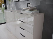 Moderne Kommode mit Hochglanzoberfläche, seitliche Perspektive, dekoriert mit Büchern und Glasvasen.