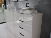 Moderne Kommode mit Hochglanzoberfläche, seitliche Perspektive, dekoriert mit Büchern und Glasvasen.