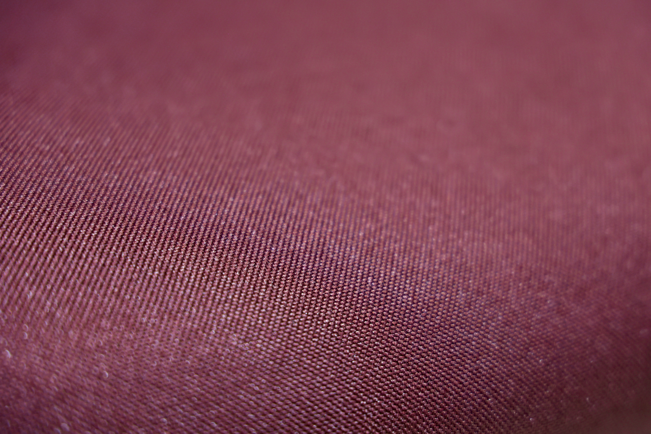 Nahaufnahme eines weinroten Stoffes, der für einen Drehstuhl verwendet wird, aus seitlicher Perspektive.