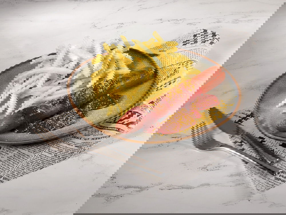 Currywurst mit Pommes auf Teller, dazu Ketchup und Currypulver, serviert auf Zeitungspapier.