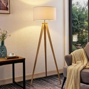 Moderne staande lamp met een houten driepoot en een ronde, witte lampenkap, gezien vanaf de zijkant in de woonkamer.