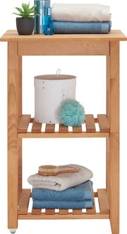 Holz-Servierwagen mit drei Ebenen, dekoriert mit Handtüchern, einer Pflanze und Pflegeprodukten, seitliche Perspektive